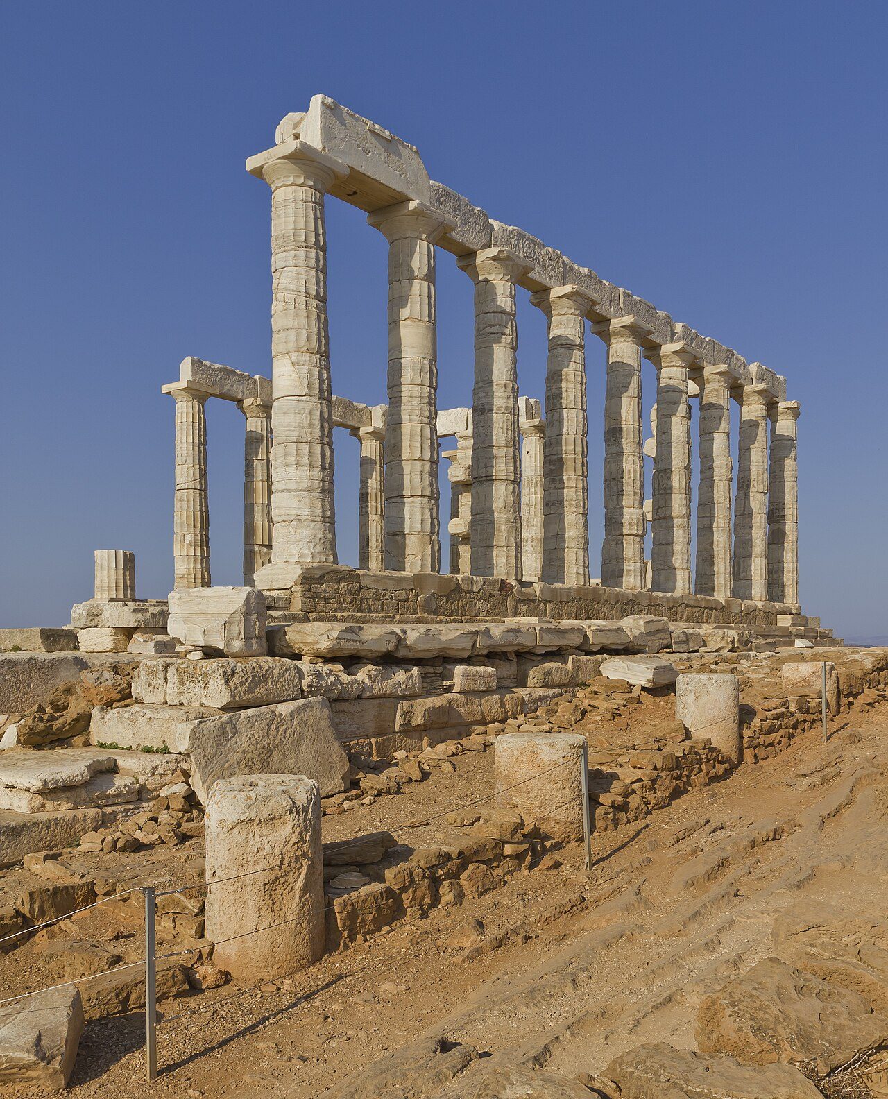 Sun-bleached classical temple ruins against a deep clear sky, wide architectural crop, desaturated with a cool navy cast